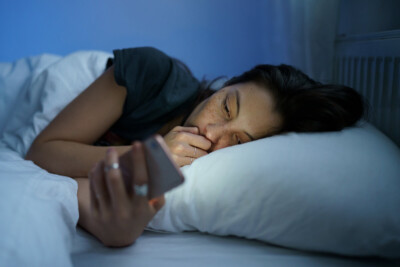 Woman laying in bed looking at her phone at night. Porn addiction therapy in Atlanta, GA can help marriages recover from this pain. A sex therapist for intimacy can help you connect again and heal together.