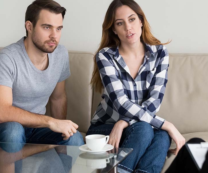 Image of two people sitting on a couch with a white teacup on a coffee table. This image illustrates what a session of discernment counseling in Atlanta, GA may look like. Couples can get help with coparenting counseling and divorce decisions from a discernment therapist here. | 30024 | 30097