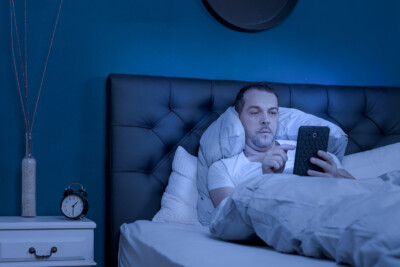 Man laying in bed, looking at something on his tablet. Porn addiction therapy in Atlanta, GA with a sex therapist for couples and marriage counseling can help you recover from this feeling of betrayal.
